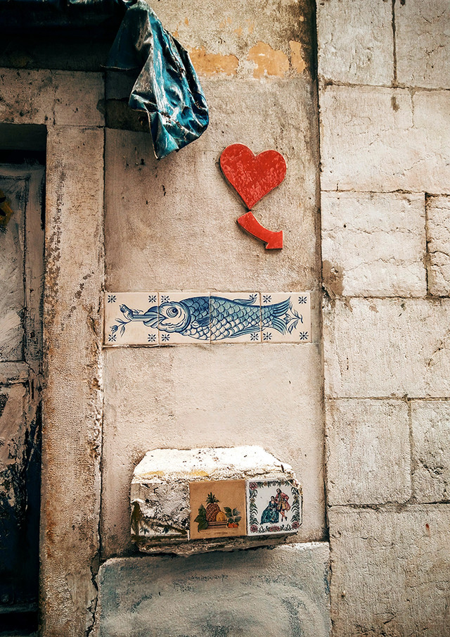 Ada Wanders/Włóczykijada. Red heart with an arrow, fish on azulejos and tiles with pictures of people and fruit in Alfama in Lisbon.